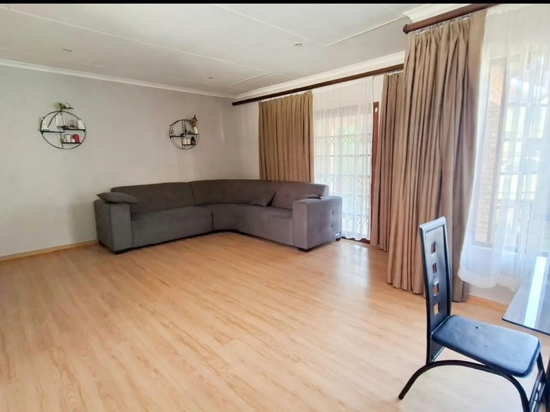 A bright living room featuring light-toned laminate flooring, coved ceilings, and a large sliding glass door providing access to the exterior.