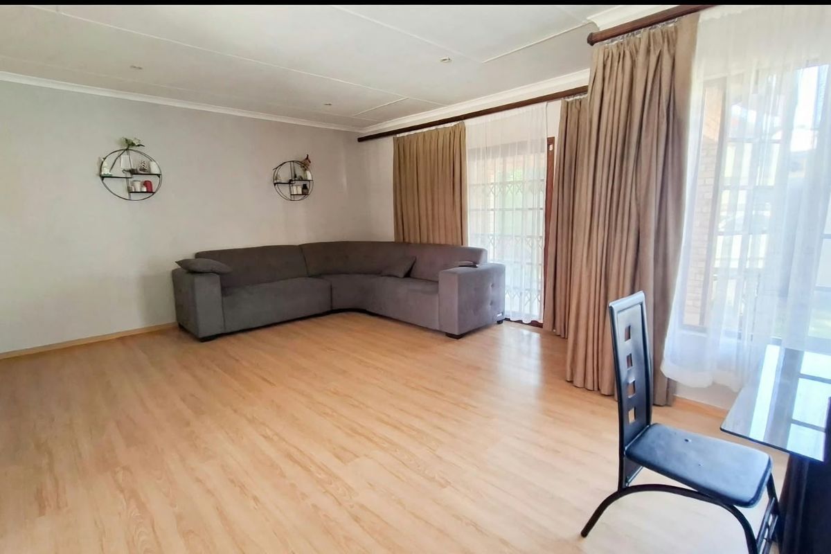 A bright living room featuring light-toned laminate flooring, coved ceilings, and a large sliding glass door providing access to the exterior.