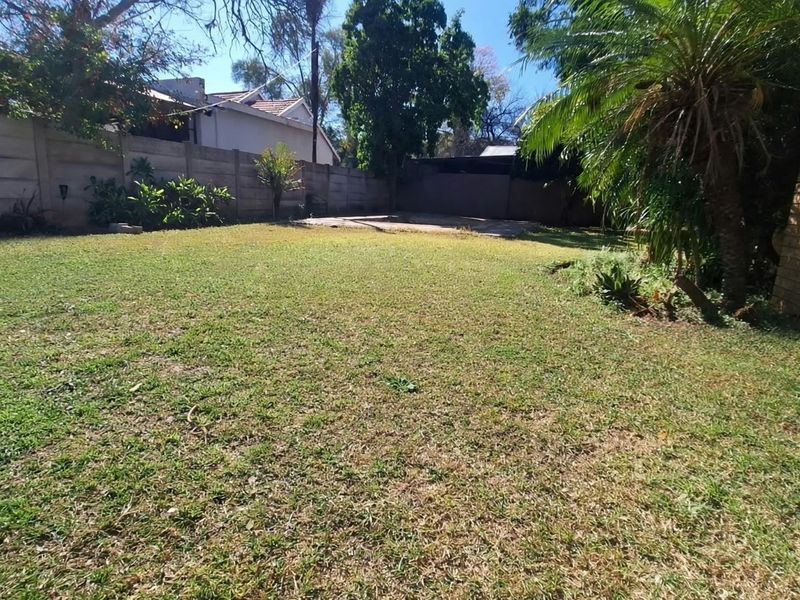A spacious private backyard featuring a large lawn area enclosed by precast concrete boundary walls and mature perimeter landscaping.