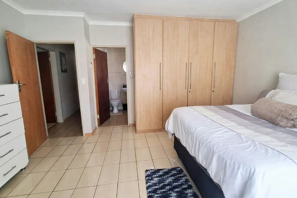 Spacious bedroom featuring light wood built-in cupboards, neutral tiled flooring, and direct access to an en-suite bathroom.