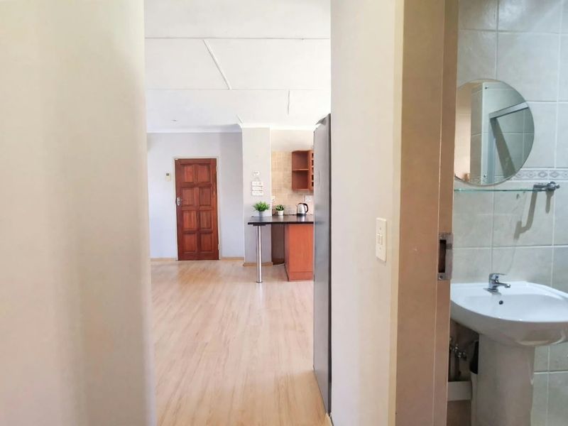 View from a bathroom doorway looking into an open-plan living and kitchen area featuring laminate flooring and neutral finishes.
