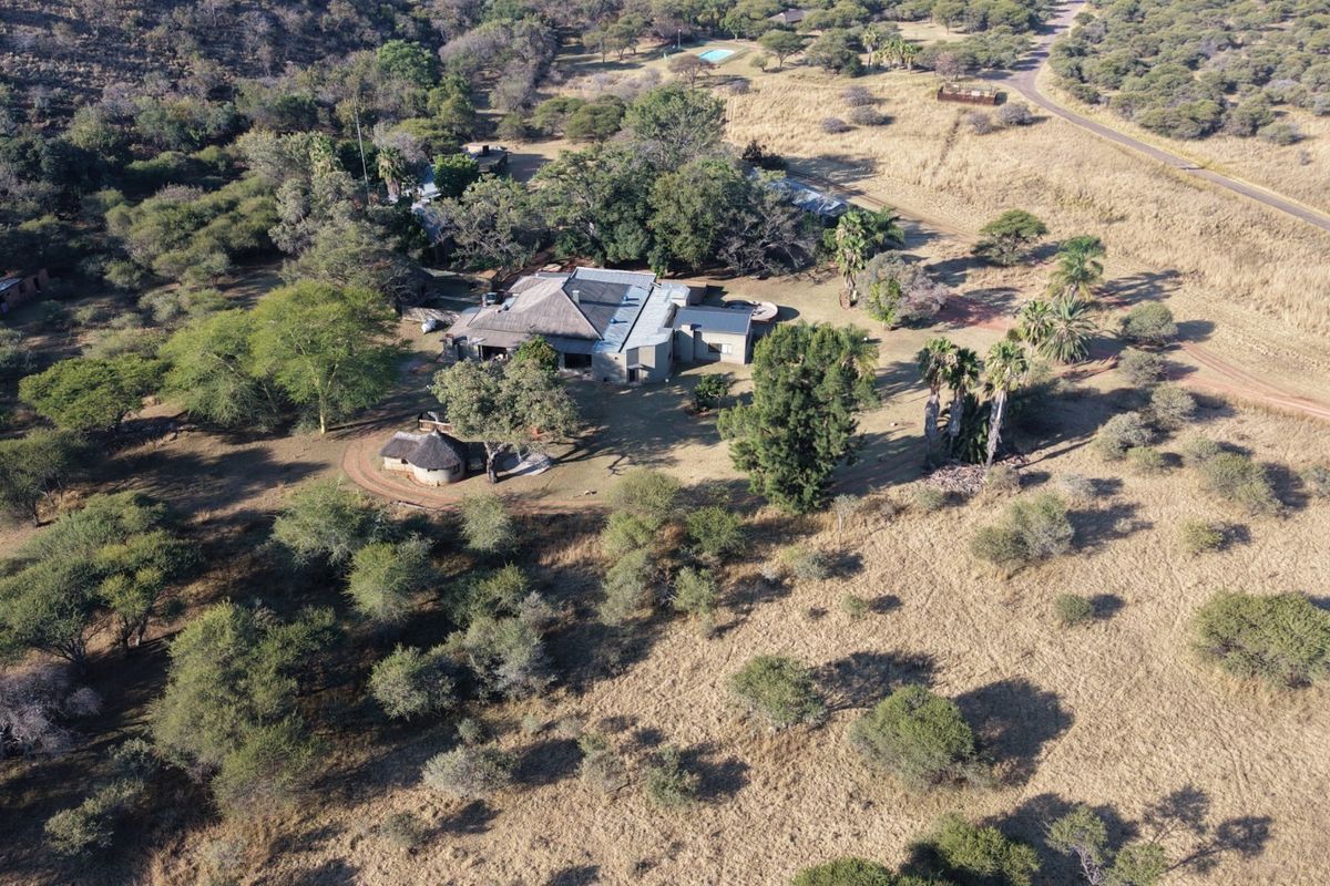 Aerial view of a lodge property featuring a thatched roof main building, swimming pool, and extensive natural grounds within a rural setting.