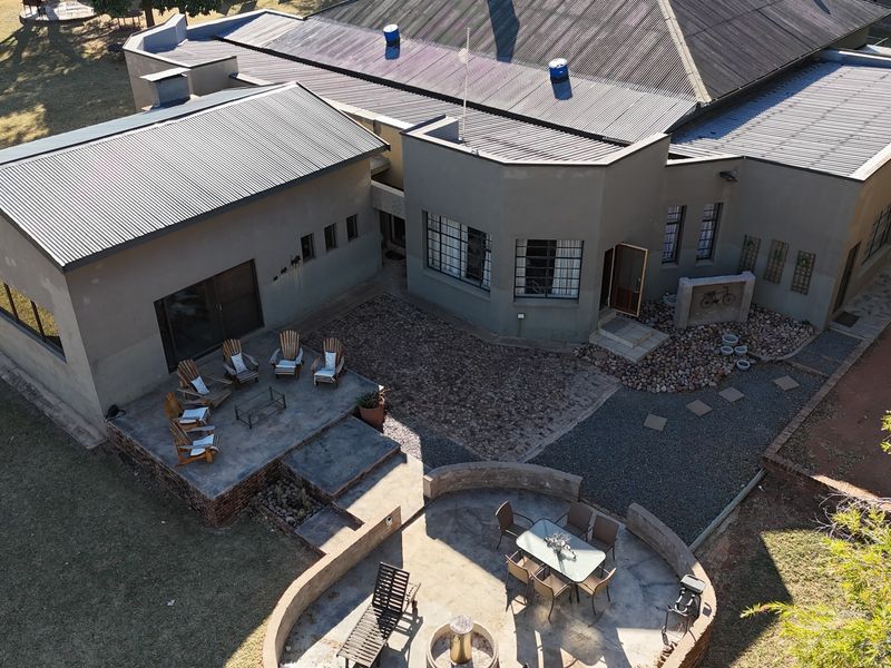Aerial view of the lodge exterior, featuring a corrugated metal roof, stone-paved patio areas, and a curved masonry retaining wall in the garden.