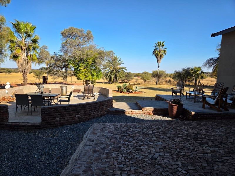 Spacious outdoor patio area featuring a curved brick retaining wall, stone paving, and gravel landscaping, overlooking a large open garden and natural landscape.