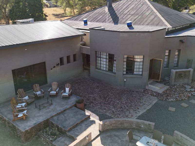 Aerial view of the lodge rear exterior, featuring a spacious concrete patio, stone-paved courtyard, and corrugated metal roofing.