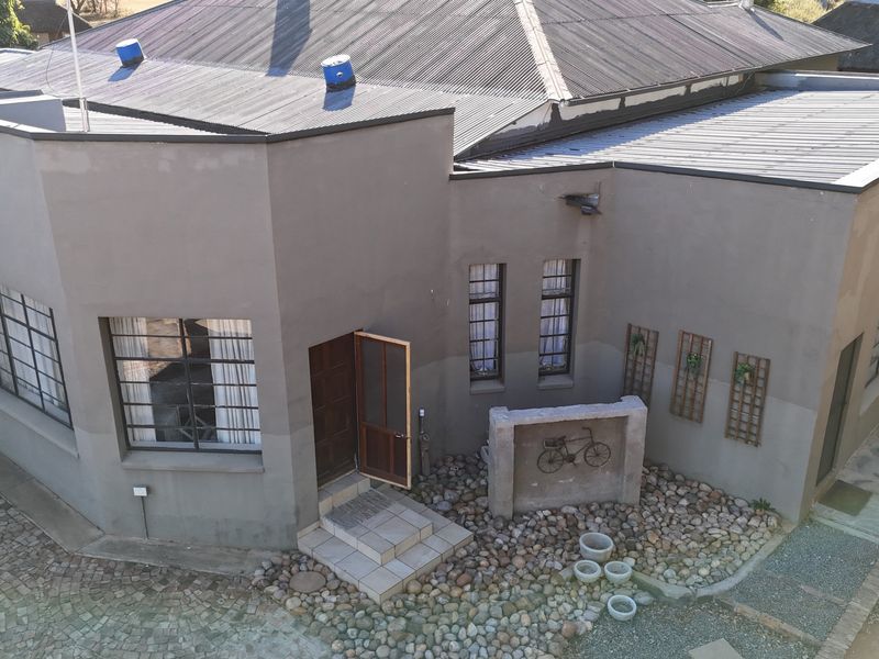Aerial view of the lodge exterior featuring a corrugated metal roof, plastered walls, and a cobblestone driveway entrance.