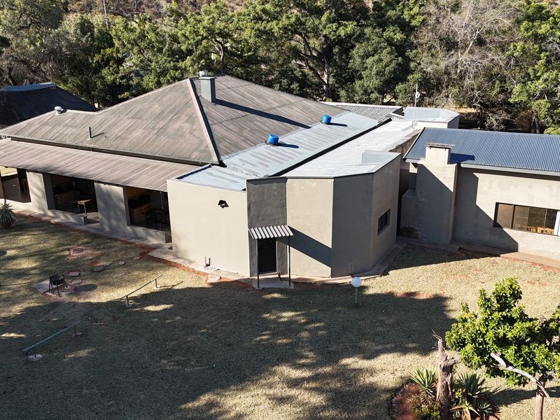 Aerial view of the lodge property featuring a large metal roof, covered patio area, and surrounding landscaped garden grounds.