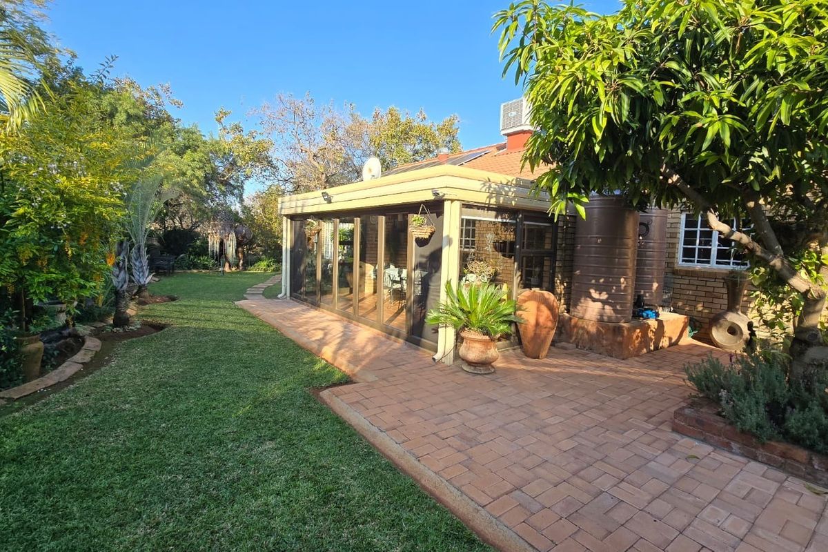 Rear view of the property featuring a paved patio area, enclosed sunroom with sliding doors, and a well-maintained garden with mature trees.