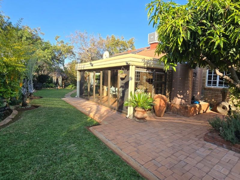 Rear view of the property featuring a paved patio area, enclosed sunroom with sliding doors, and a well-maintained garden with mature trees.