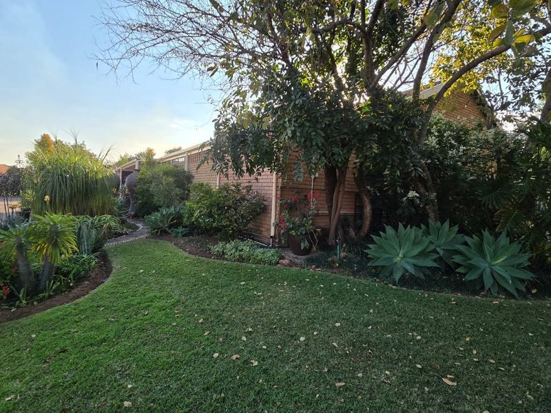 A view of the rear brick facade of the house, featuring a well-maintained garden with mature trees and a paved pathway.