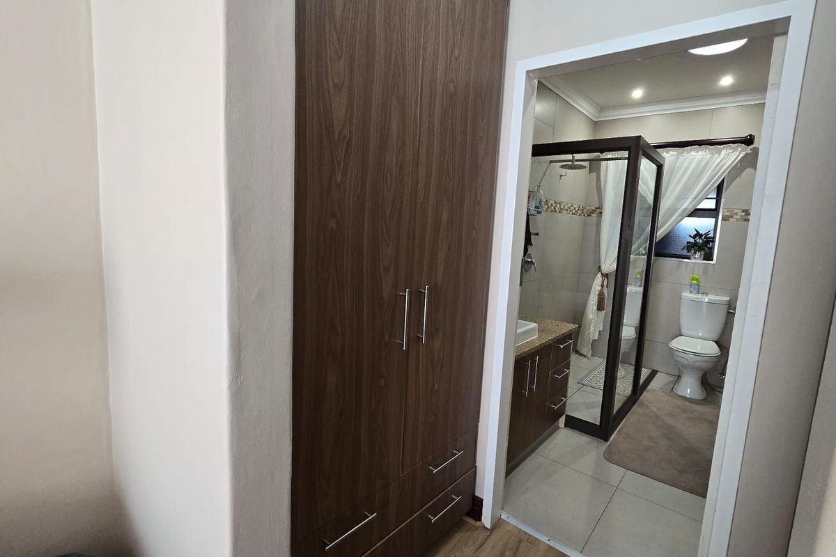A well-maintained bathroom featuring a modern shower enclosure, vanity cabinet with basin, and built-in storage cupboards in the adjacent hallway area.