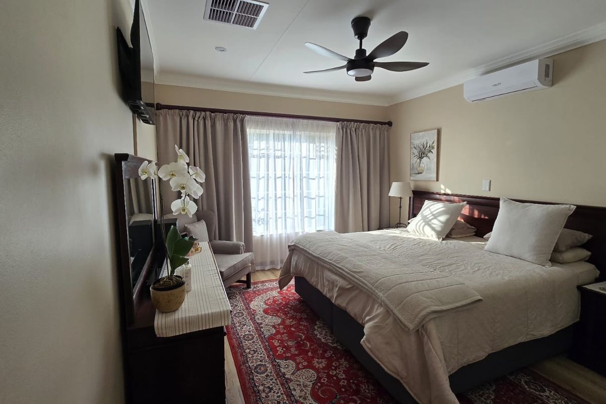 A well-maintained bedroom featuring a ceiling fan, split system air conditioning, and neutral wall finishes with coving detail.
