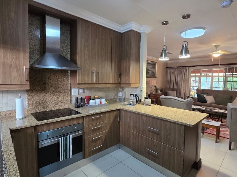 Open-plan kitchen featuring wood-finish cabinetry, granite countertops, and integrated appliances, flowing seamlessly into a comfortable living area with tiled floors.