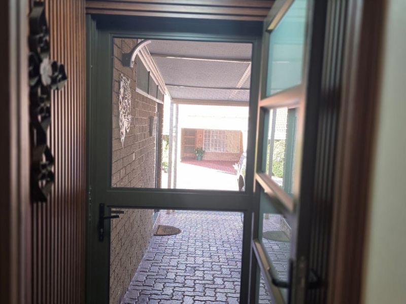 View from the interior looking out through a security screen door towards a paved driveway and carport area.
