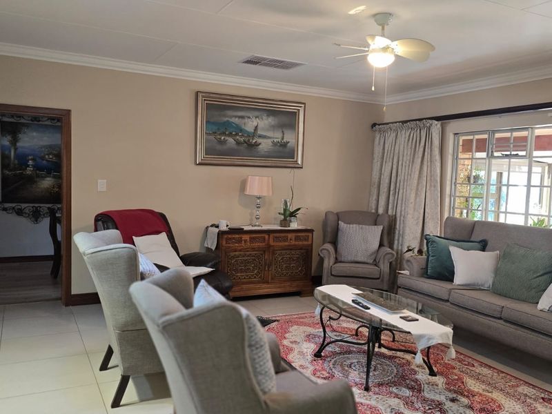 A comfortable living room featuring tiled flooring, coved cornicing, a ceiling fan, and a sliding glass door providing access to the outdoor area.