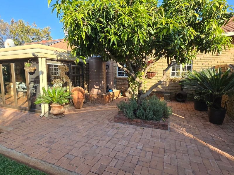 A well-maintained rear garden area featuring brick paving, a mature tree in a raised planter, and an enclosed patio structure.