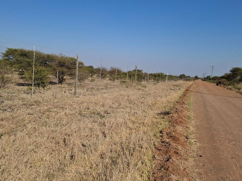 A view of a dirt road bordering a vacant residential plot featuring wire fencing and native vegetation.