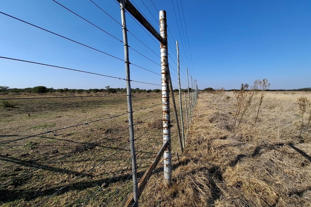 A view of the vacant land perimeter featuring wire fencing with visible signs of corrosion on the metal support posts.