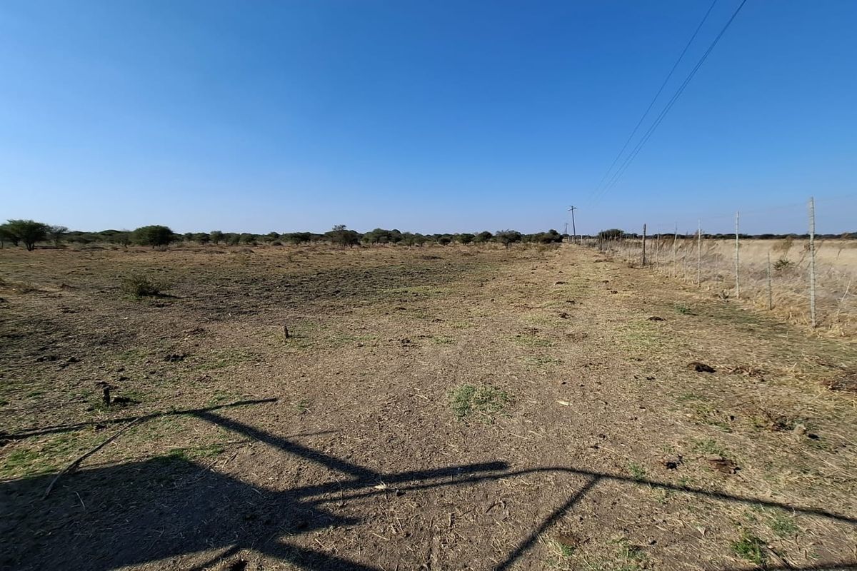 A wide-angle view of a vacant residential plot featuring natural terrain and perimeter wire fencing under a clear blue sky.