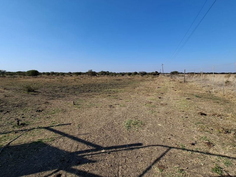 A wide-angle view of a vacant residential plot featuring natural terrain and perimeter wire fencing under a clear blue sky.