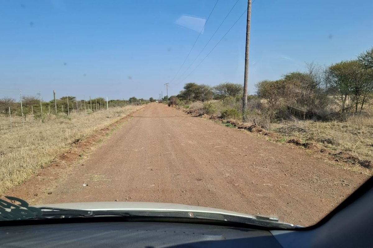 A view of an unpaved dirt road leading towards the property, featuring surrounding natural vegetation and utility infrastructure.