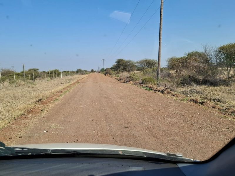 A view of an unpaved dirt road leading towards the property, featuring surrounding natural vegetation and utility infrastructure.