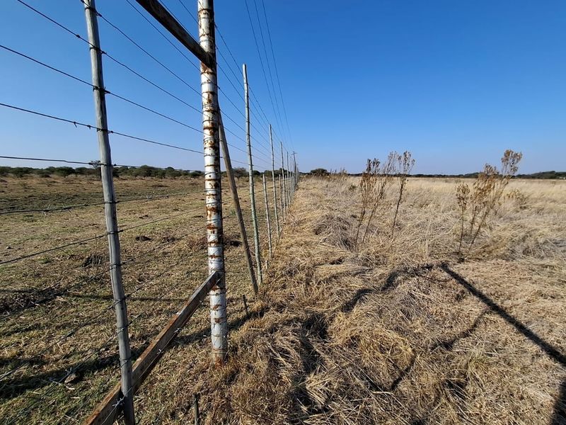 A view of the property boundary featuring a wire fence with metal posts running along the edge of the vacant residential land.