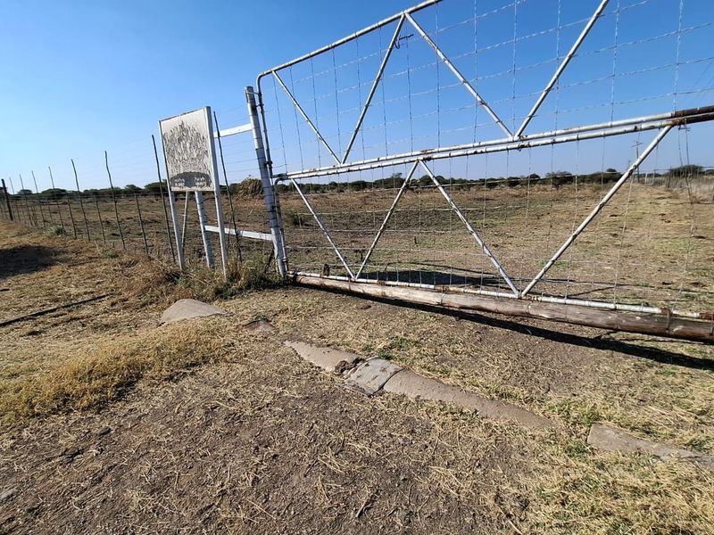 A view of the property entrance featuring a metal farm gate and wire mesh fencing surrounding the vacant residential land.