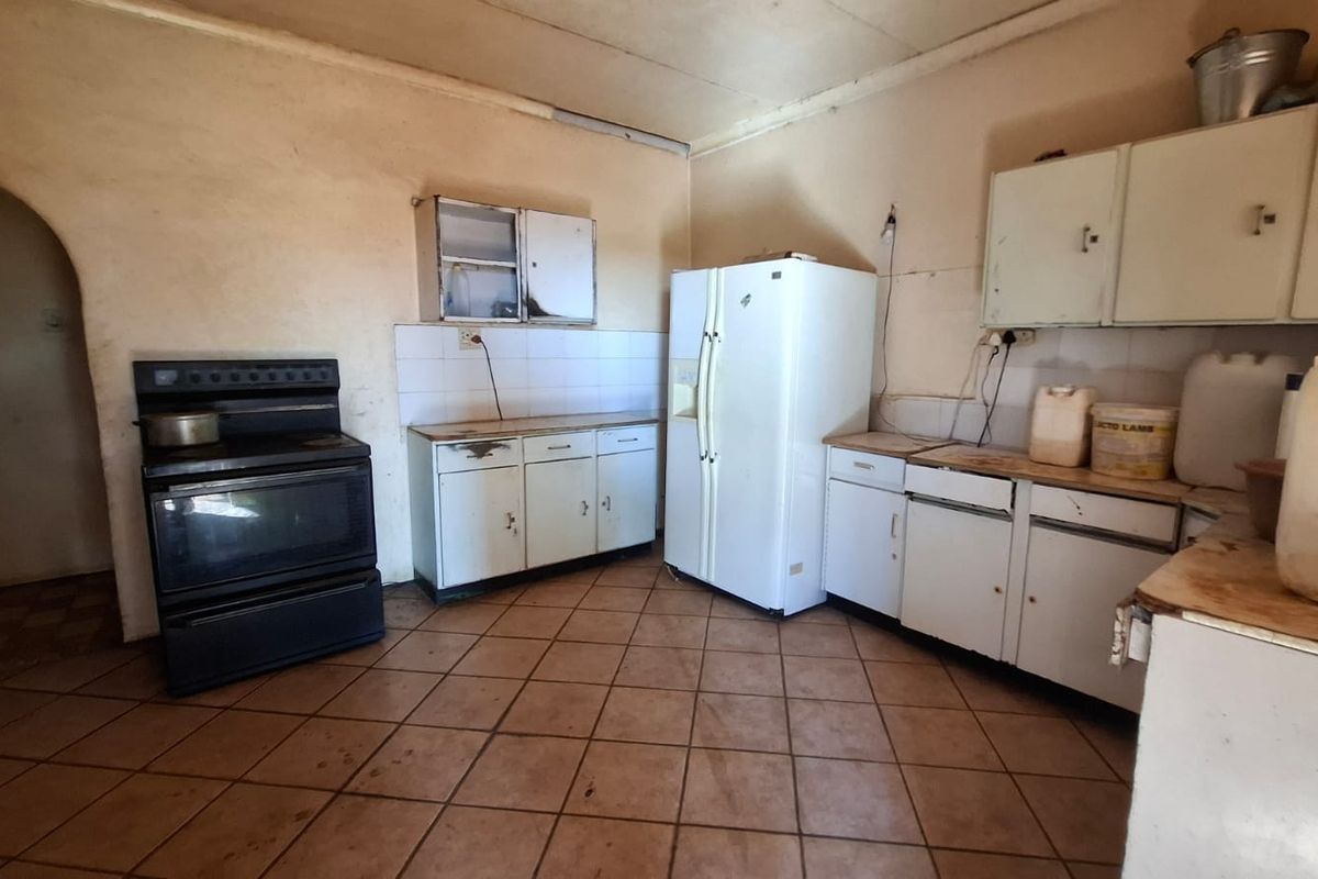 A dated kitchen featuring original cabinetry, tiled flooring, and a tiled splashback, requiring significant renovation to modernize the space.