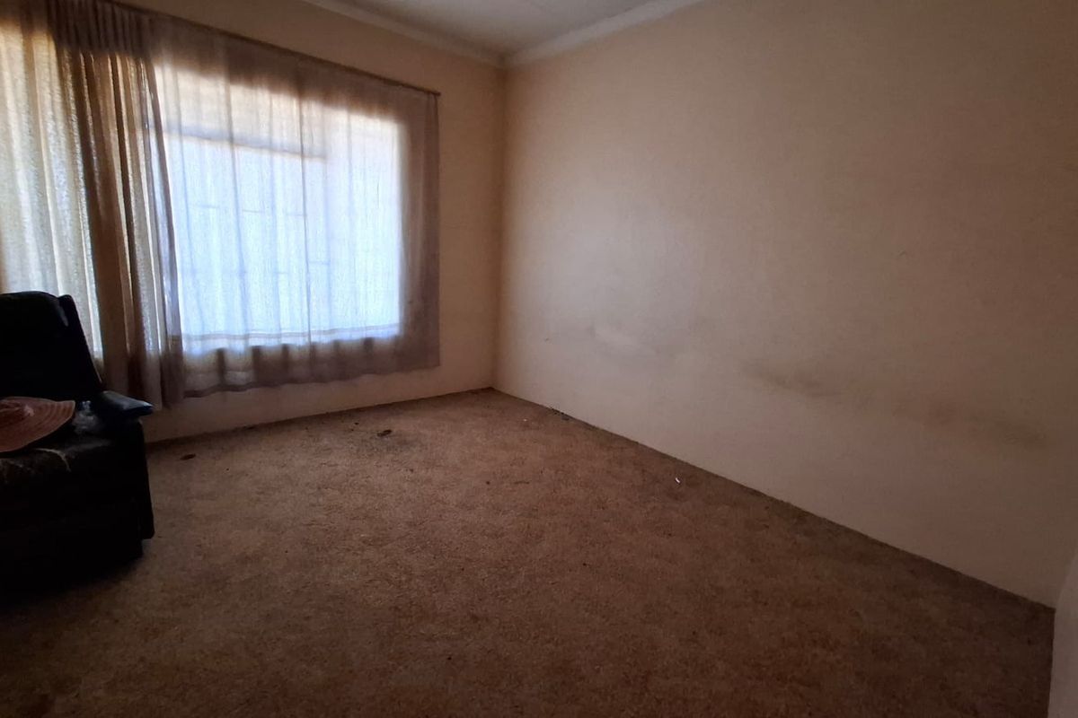 A vacant bedroom featuring carpeted flooring and a large window with curtain rails, requiring cosmetic updates to the walls and flooring.