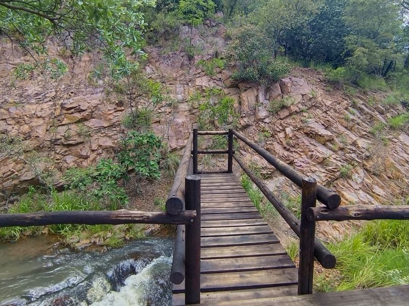 A scenic wooden footbridge crossing a natural stream, set against a rugged rock face in a tranquil outdoor setting.