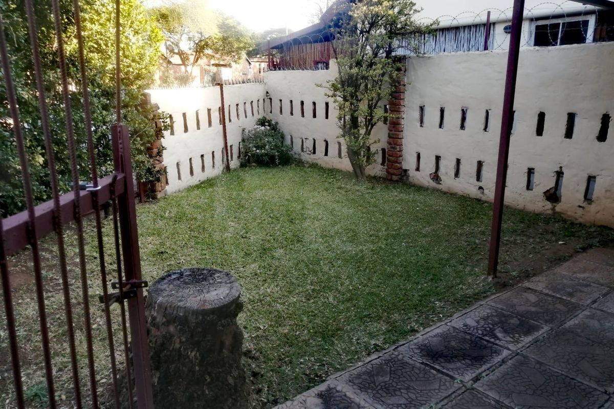 A private garden area featuring a lawn, paved patio section, and secure perimeter wall with razor wire fencing.