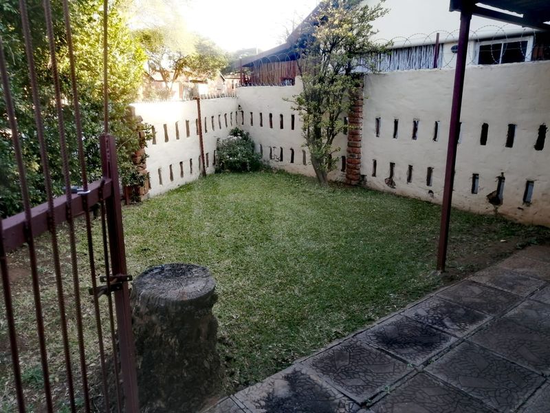 A private garden area featuring a lawn, paved patio section, and secure perimeter wall with razor wire fencing.