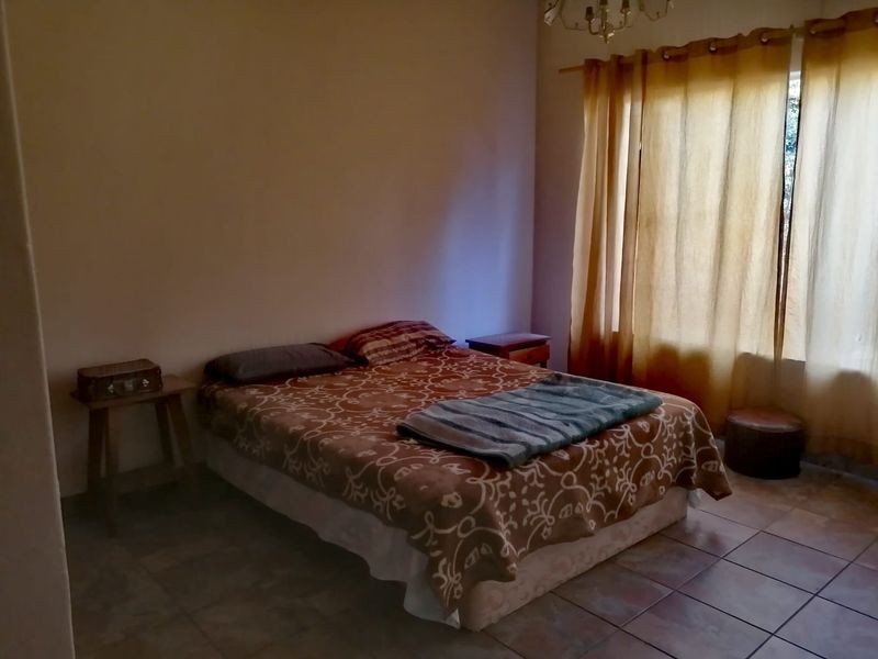 A bedroom featuring tiled flooring and natural light through window curtains.