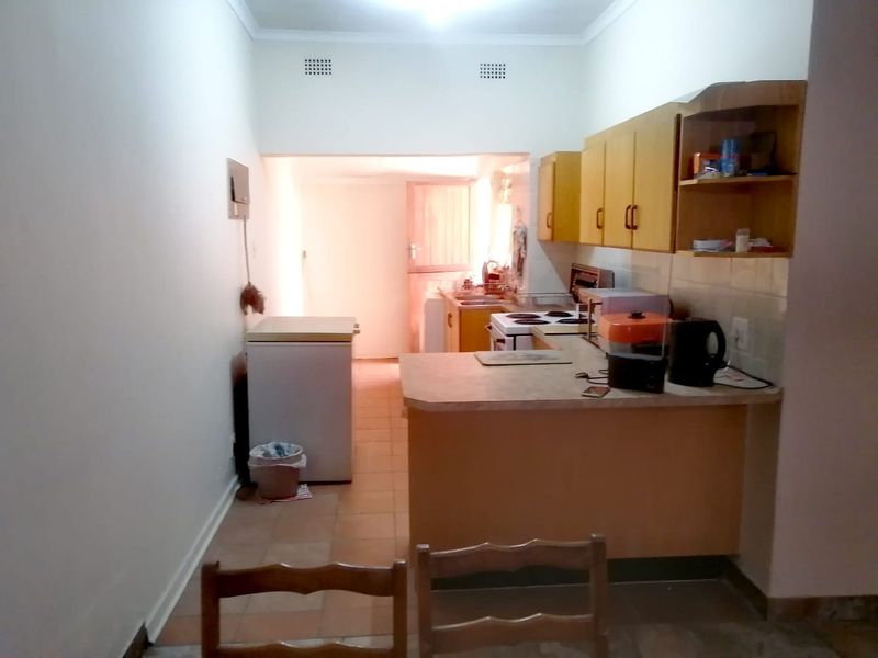 A functional kitchen featuring dated cabinetry, laminate countertops, and an electric stove, with a tiled floor and direct access to a rear utility area.