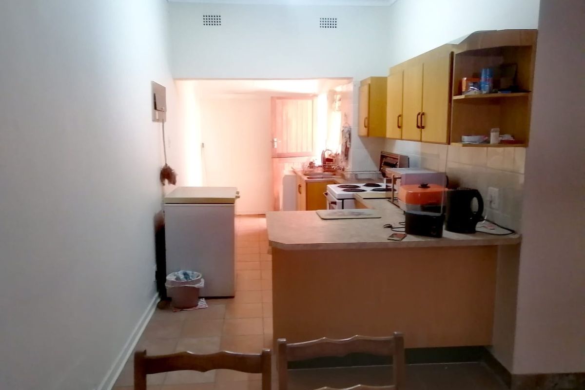 A functional kitchen featuring dated cabinetry, laminate countertops, and an electric stove, with a tiled floor and direct access to a rear utility area.