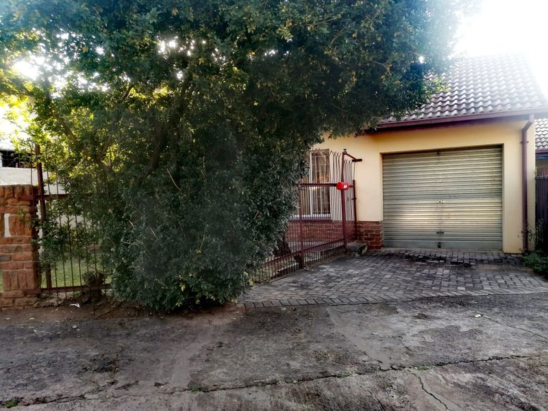 Front exterior view of the townhouse featuring a roller shutter garage door, paved driveway, and metal security gate entrance.
