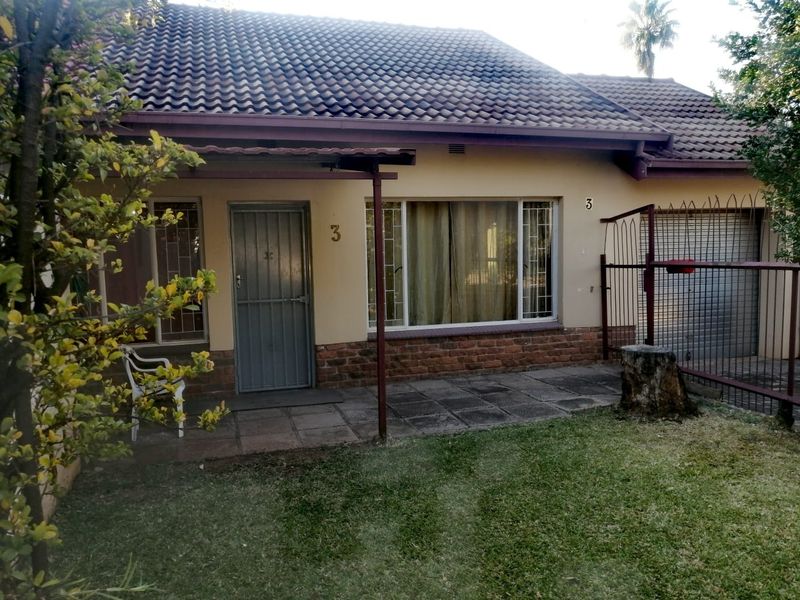 Front elevation of a townhouse featuring a tiled roof, brick facade, paved patio area, and an integrated garage with security fencing.