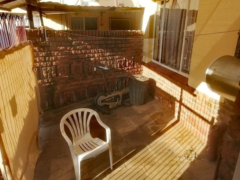 A compact, paved outdoor patio area featuring a brick boundary wall and an external geyser, offering a functional space for laundry or utility use.