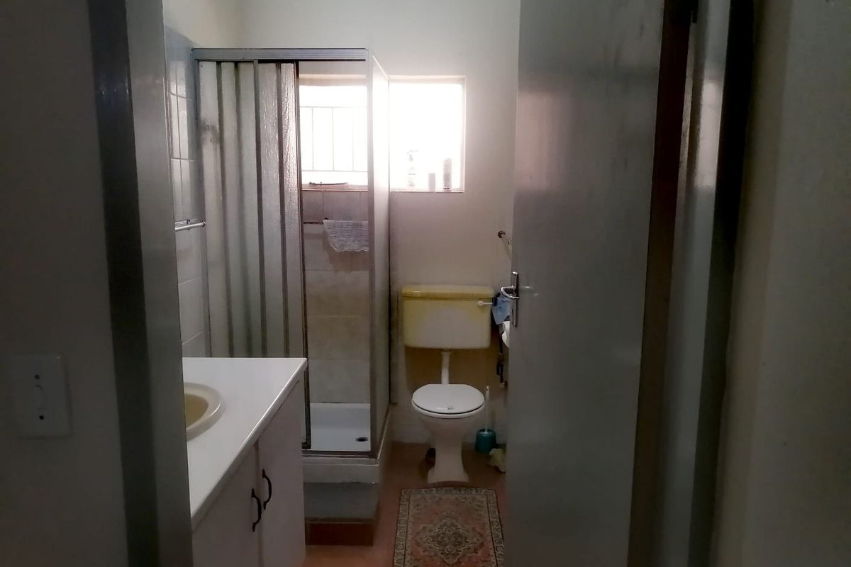 A functional bathroom featuring a shower enclosure, vanity cabinet with basin, and toilet, requiring cosmetic updates to modernize the space.
