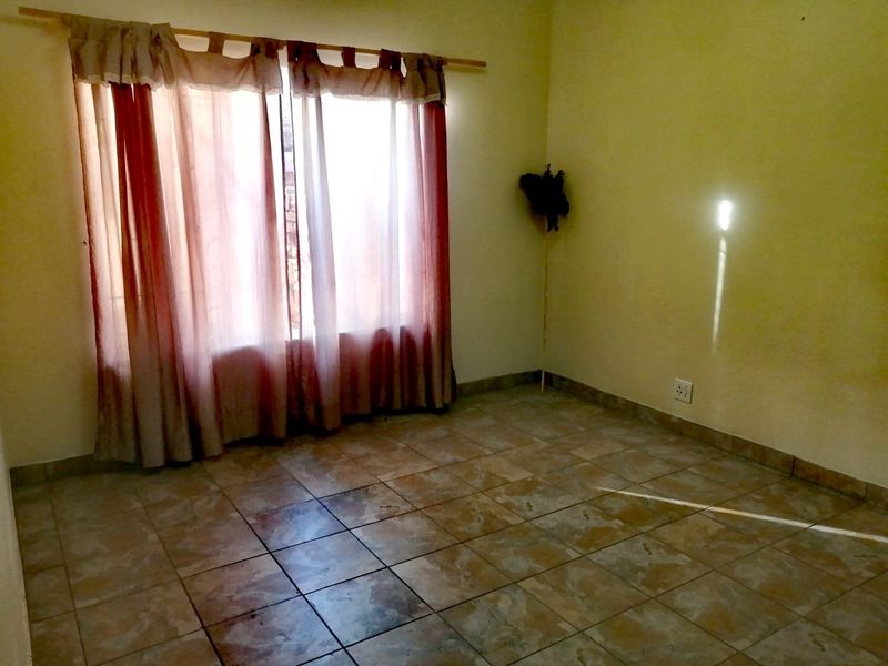 An empty bedroom featuring tiled flooring and a large window with a curtain rod, providing a blank canvas for potential interior design updates.