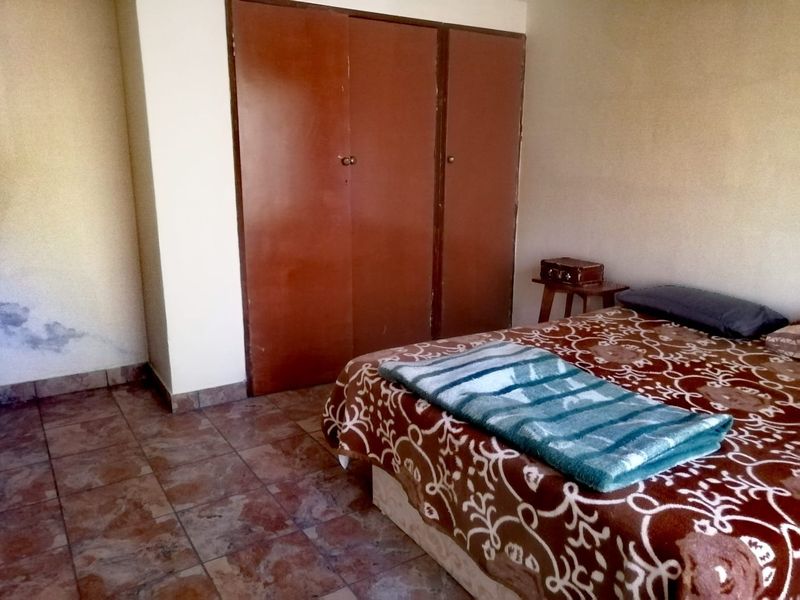 Bedroom featuring built-in cupboards and tiled flooring. The room requires cosmetic updates to address wall staining and improve overall finish.
