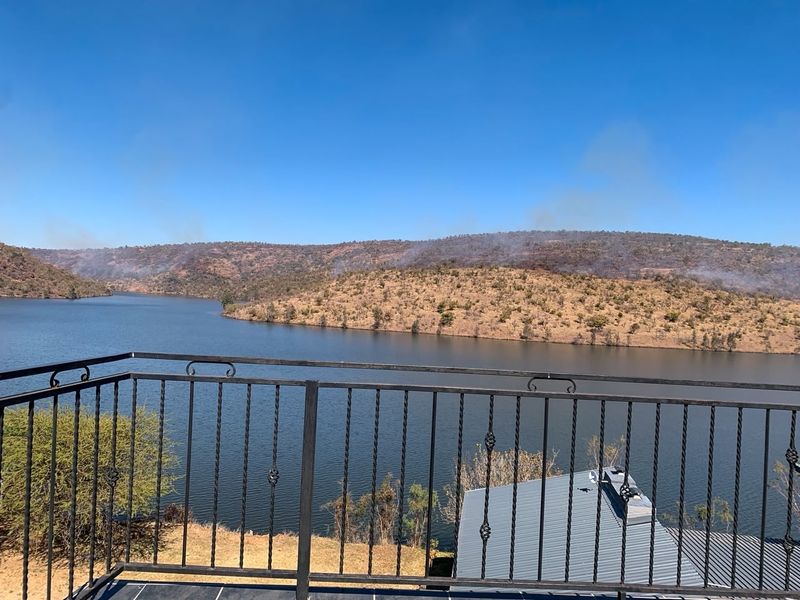 A scenic elevated view overlooking a large dam or lake, framed by a black wrought iron balcony railing.