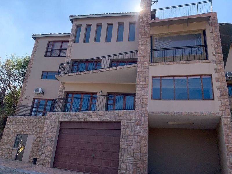 Multi-story residential facade featuring stone cladding, multiple balconies with wrought iron railings, timber window frames, and an integrated garage.