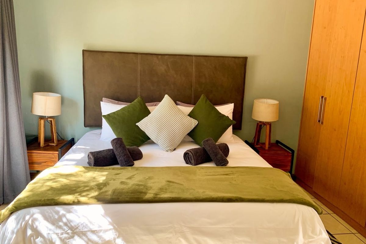 A well-maintained bedroom featuring a built-in wardrobe, tiled flooring, and a neutral green accent wall.
