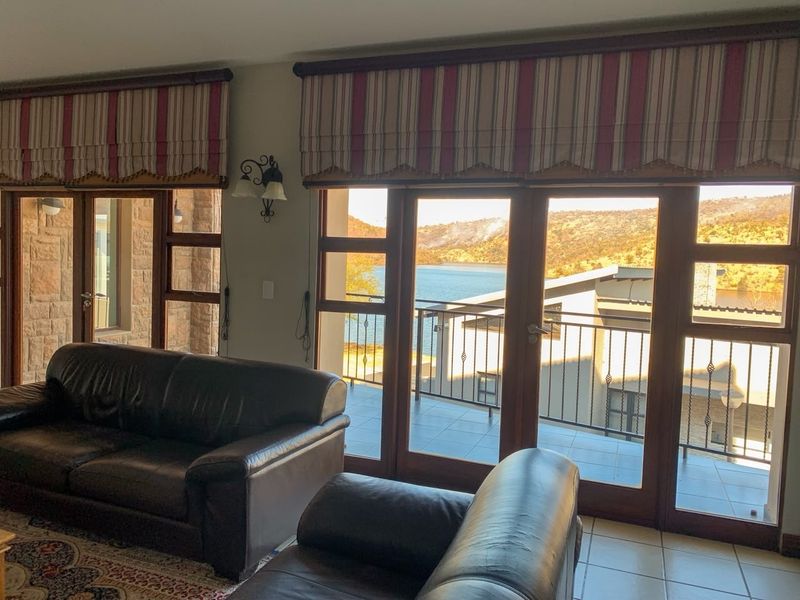 Spacious living room featuring large wooden-framed glass doors that open onto a balcony with scenic water views.