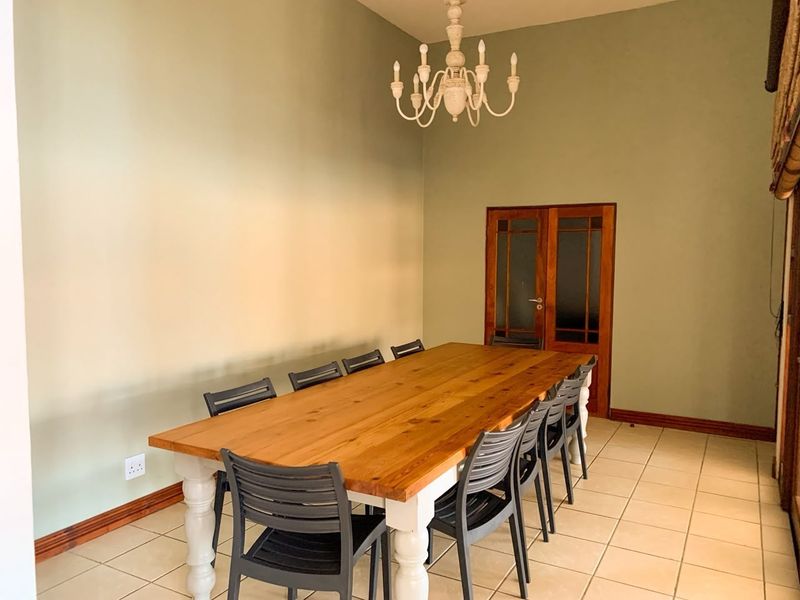 A spacious dining room featuring neutral-toned walls, tiled flooring, and a classic chandelier, providing a functional space for family meals and entertaining.