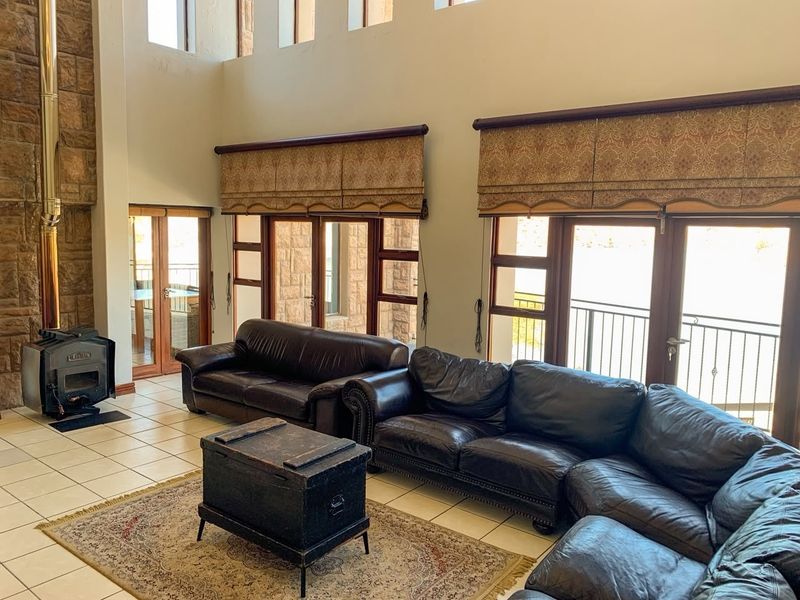 Spacious living room featuring a stone fireplace with a wood-burning stove, high ceilings, tiled floors, and multiple glass doors leading to a balcony.