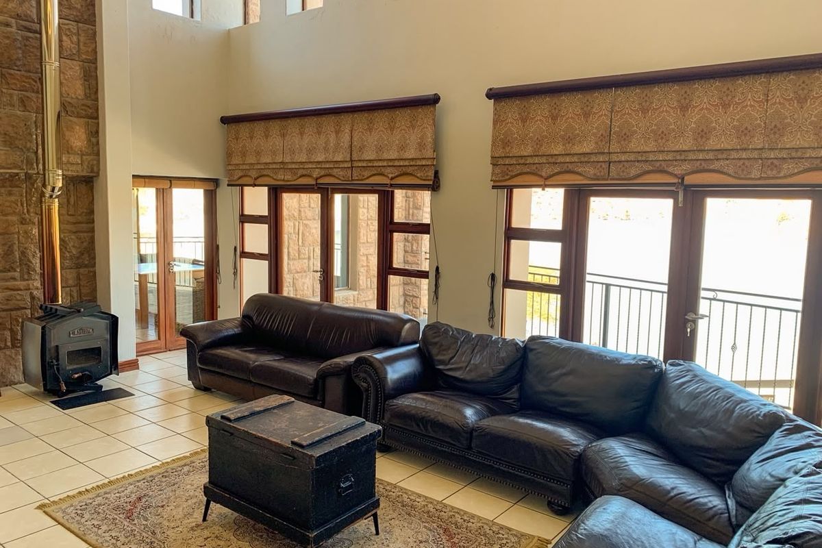 Spacious living room featuring a stone fireplace with a wood-burning stove, high ceilings, tiled floors, and multiple glass doors leading to a balcony.