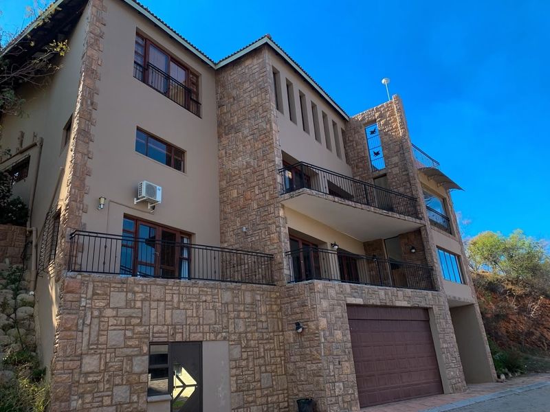 A multi-story residential facade featuring stone cladding, multiple balconies with wrought iron railings, and an integrated garage.
